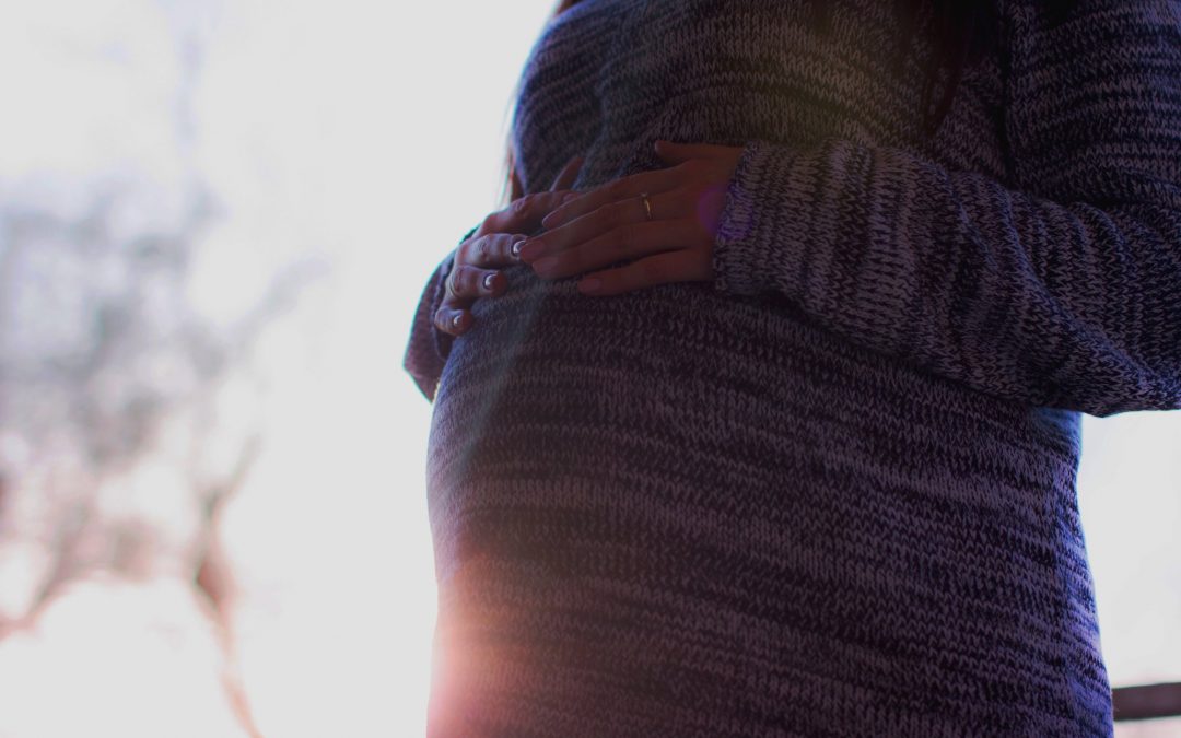 close up of pregnant woman wearing sweater and touching her stomach